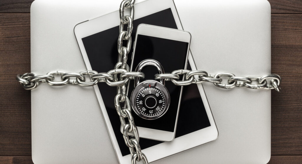 data security concept: computer, tablet, phone bound by metal chain and closed with combination lock on wooden table