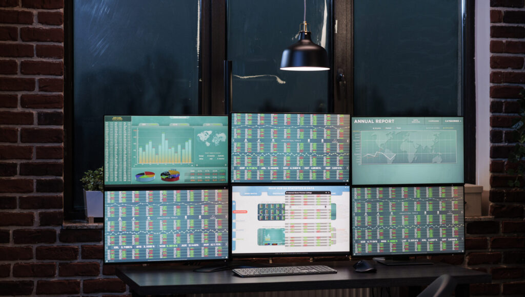 Empty trade office with nobody in it with screens showing financial information and real time data. Interior of forex stock market workstation with multiple monitors and economic charts on displays.